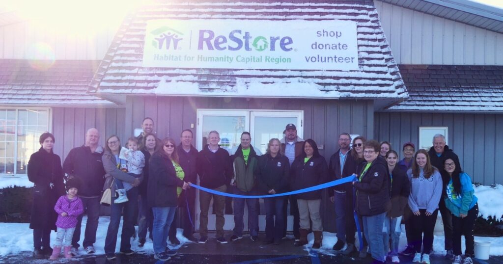 Shoppers, the St. Johns Mayor and Chamber, volunteers, and staff pose for a group photo behind the ribbon before the ceremony.