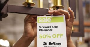 A women hangs up a clearance tag for the ReStore Sidewalk Sales.